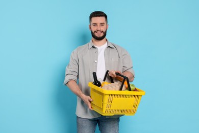 Photo of Man with shopping basket full of products on light blue background