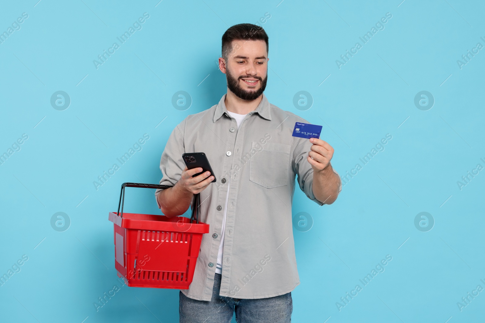 Man with empty shopping basket and credit card on light blue background Photo of Man with empty shopping basket and credit card on light blue background