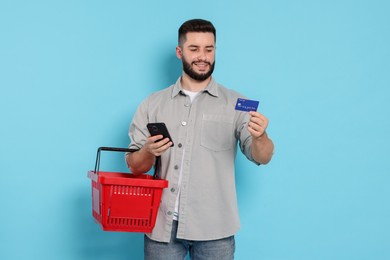 Photo of Man with empty shopping basket and credit card on light blue background