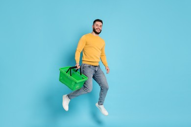 Photo of Man with empty shopping basket jumping on light blue background