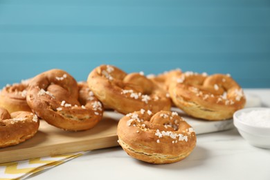 Photo of Tasty pretzels with salt on white marble table, closeup