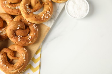 Photo of Tasty pretzels with salt on white marble table, flat lay. Space for text