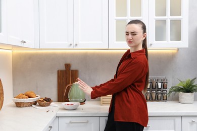 Photo of Emotional woman afraid of cockroaches in kitchen. Pest problem