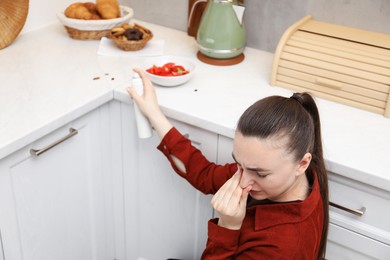 Photo of Woman spraying insecticide onto cockroaches in kitchen