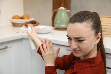 Photo of Woman spraying insecticide onto cockroaches in kitchen, selective focus
