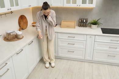 Photo of Woman spraying insecticide onto cockroaches on floor in kitchen. Pest problem
