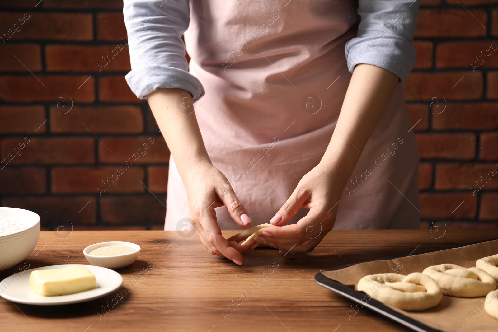 Woman shaping pretzels at wooden table, closeup Photo of Woman shaping pretzels at wooden table, closeup