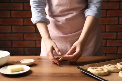 Photo of Woman shaping pretzels at wooden table, closeup