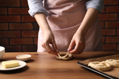 Photo of Woman shaping pretzels at wooden table, closeup