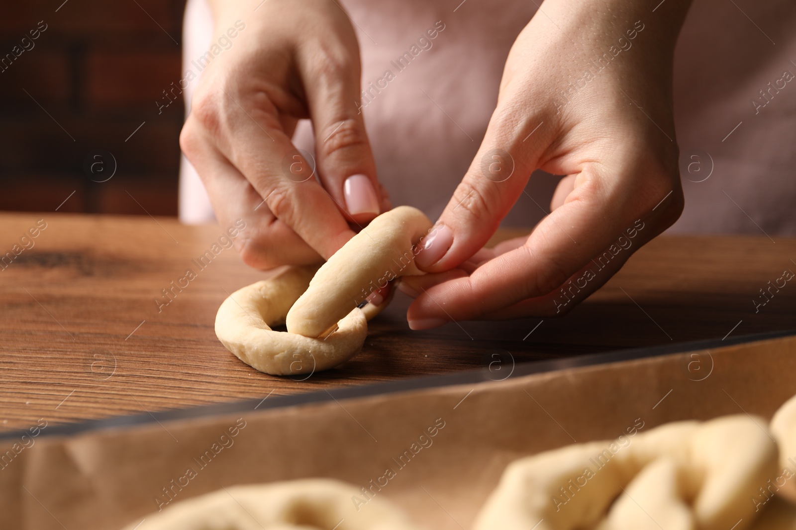 Woman shaping pretzels at wooden table, closeup Photo of Woman shaping pretzels at wooden table, closeup
