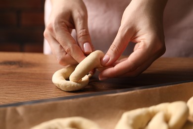 Photo of Woman shaping pretzels at wooden table, closeup