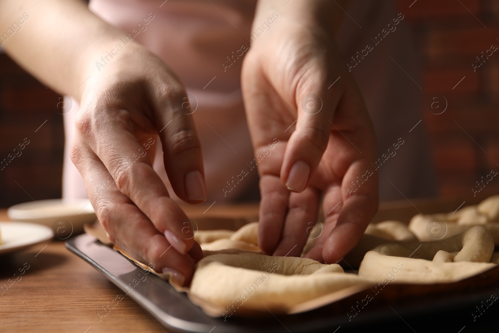 Woman putting uncooked pretzel onto baking dish at wooden table, closeup Photo of Woman putting uncooked pretzel onto baking dish at wooden table, closeup