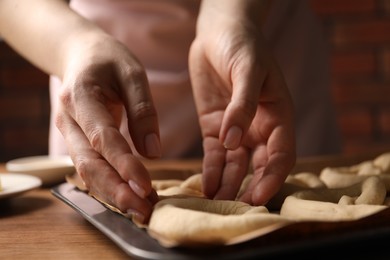 Photo of Woman putting uncooked pretzel onto baking dish at wooden table, closeup