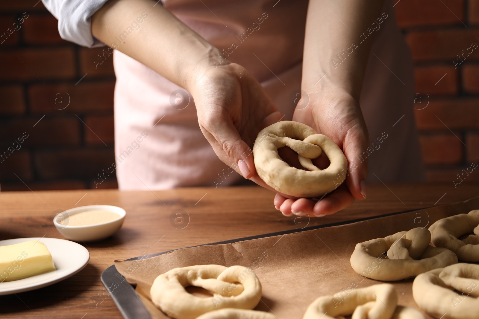 Woman putting uncooked pretzel onto baking dish at wooden table, closeup Photo of Woman putting uncooked pretzel onto baking dish at wooden table, closeup