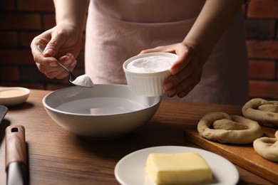 Photo of Making pretzels. Woman adding baking soda into bowl of water at wooden table, closeup