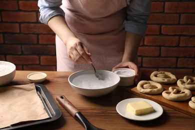 Photo of Making pretzels. Woman adding baking soda into bowl of water at wooden table, closeup