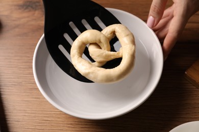Photo of Woman putting uncooked pretzel into bowl of water at wooden table, closeup