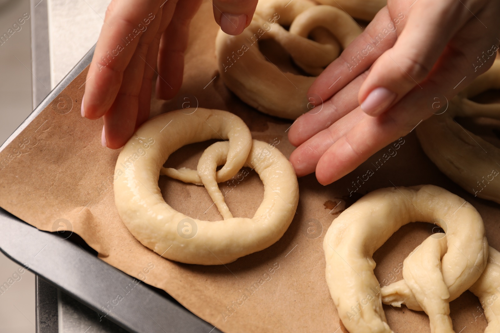 Woman putting uncooked pretzel onto baking dish at table, closeup Photo of Woman putting uncooked pretzel onto baking dish at table, closeup