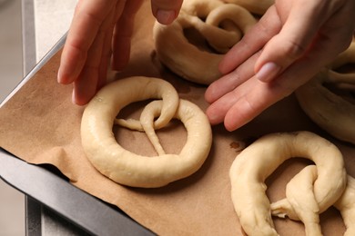 Photo of Woman putting uncooked pretzel onto baking dish at table, closeup