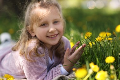 Photo of Cute little girl among beautiful dandelions outdoors on sunny day