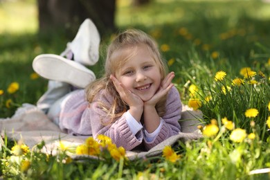 Photo of Cute little girl among beautiful dandelions on green grass outdoors