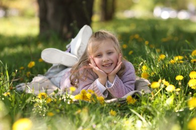 Photo of Cute little girl among beautiful dandelions on green grass outdoors