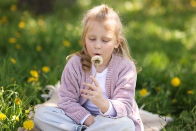 Photo of Cute little girl blowing beautiful dandelion on green grass outdoors