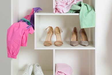 Photo of Shelving unit with different footwear and clothes indoors. Shoe storage