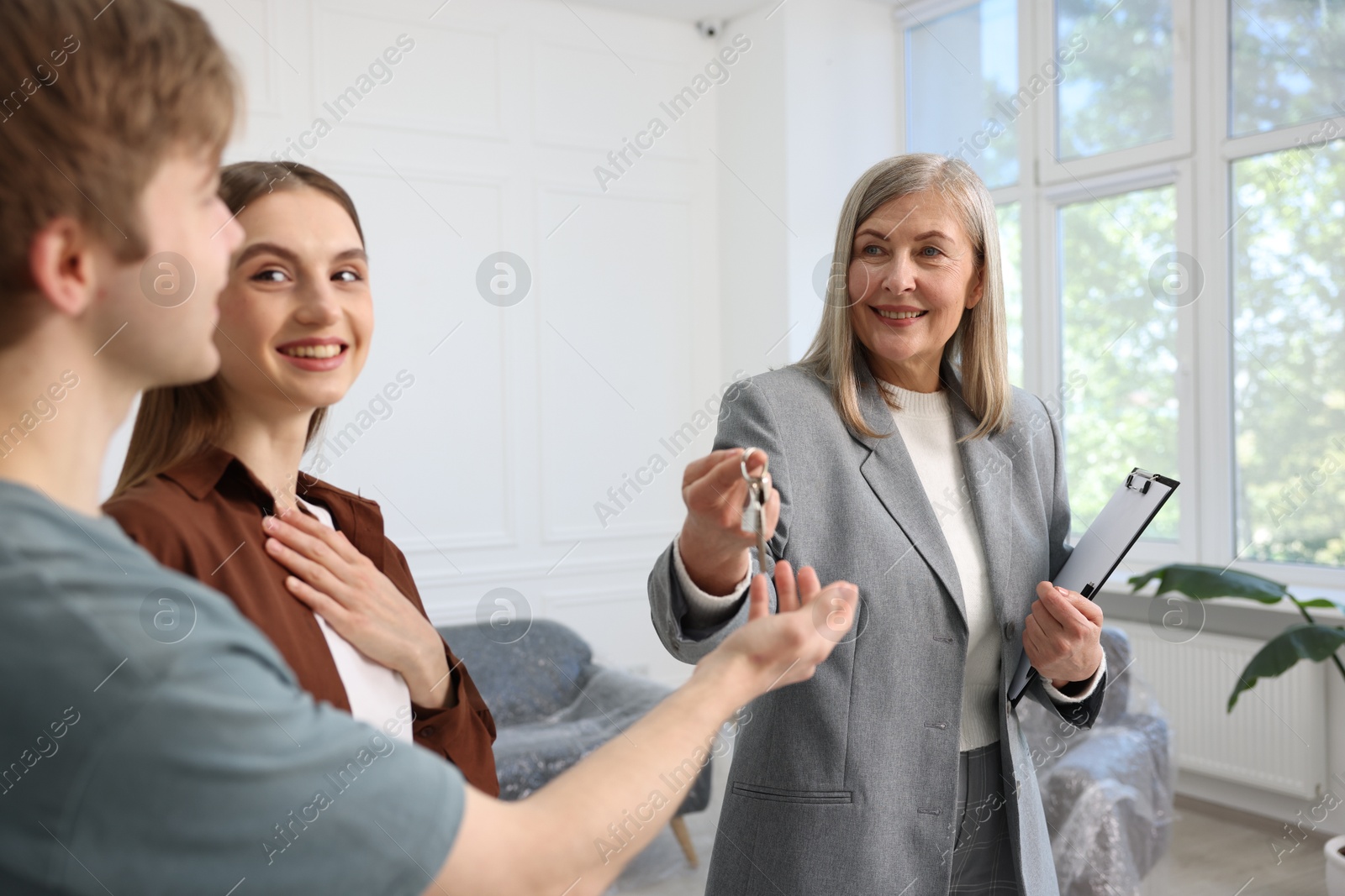 Smiling real estate agent giving house key to new owner indoors, selective focus Photo of Smiling real estate agent giving house key to new owner indoors, selective focus