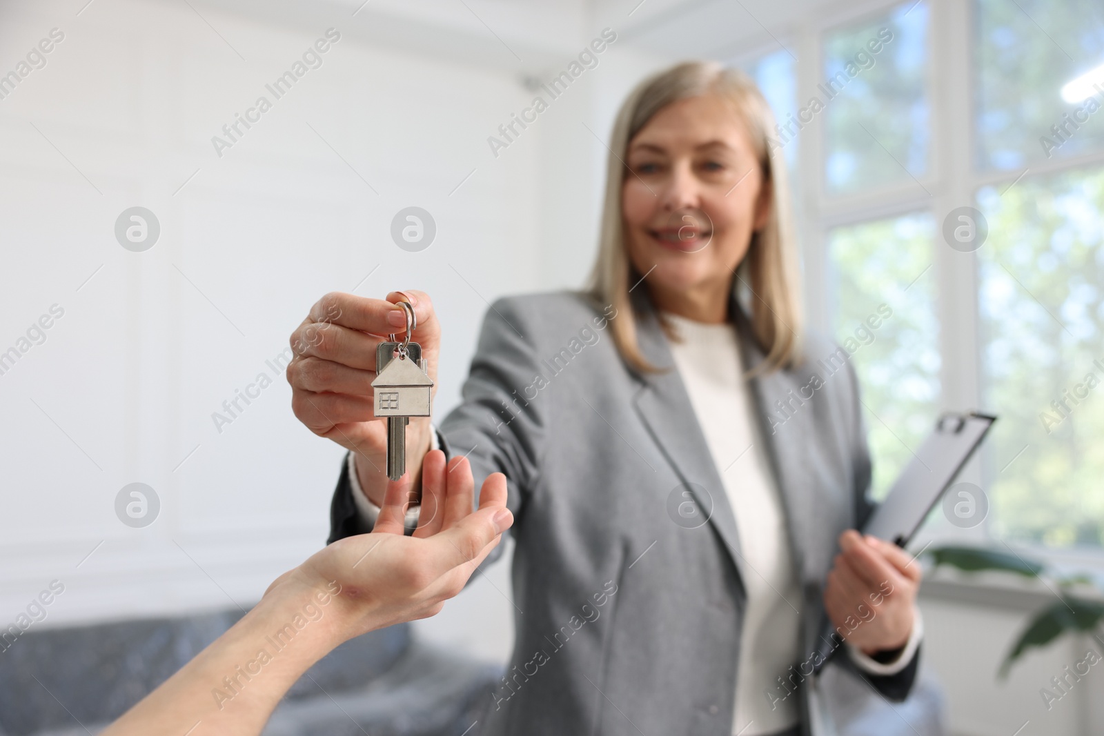 Smiling real estate agent giving house key to new owner indoors, selective focus Photo of Smiling real estate agent giving house key to new owner indoors, selective focus