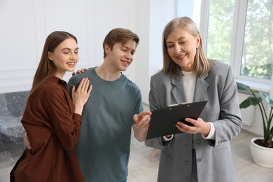 Photo of Smiling real estate agent with clipboard working with couple at home