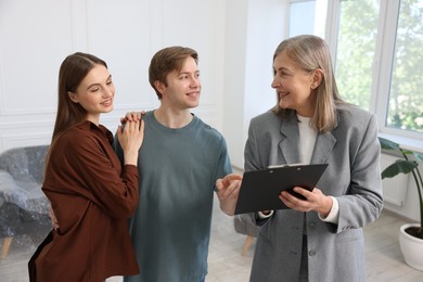 Photo of Smiling real estate agent with clipboard working with couple at home