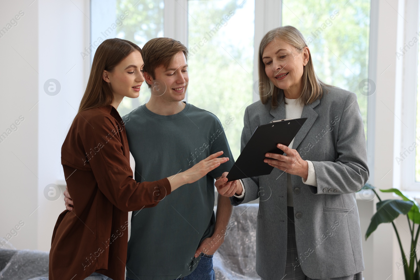 Smiling real estate agent with clipboard working with couple at home Photo of Smiling real estate agent with clipboard working with couple at home
