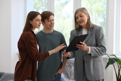 Photo of Smiling real estate agent with clipboard working with couple at home