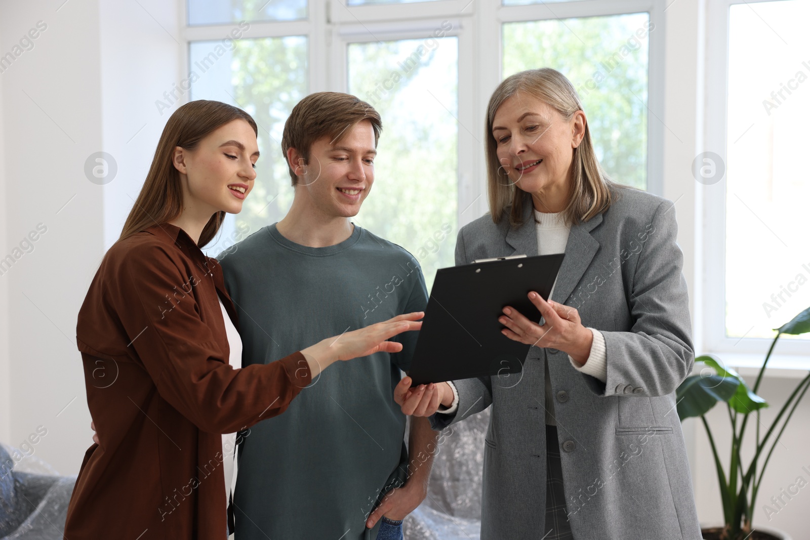 Smiling real estate agent with clipboard working with couple at home Photo of Smiling real estate agent with clipboard working with couple at home