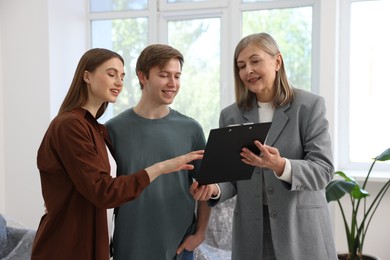 Photo of Smiling real estate agent with clipboard working with couple at home