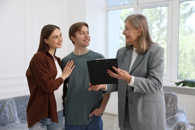 Photo of Smiling real estate agent with clipboard working with couple at home