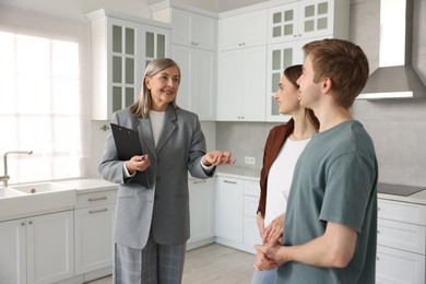 Photo of Smiling real estate agent with tablet working with couple in kitchen