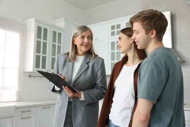 Photo of Smiling real estate agent with clipboard working with couple in kitchen