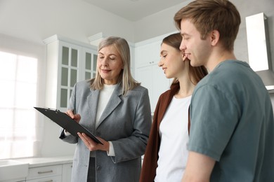 Photo of Real estate agent with clipboard working with couple in kitchen