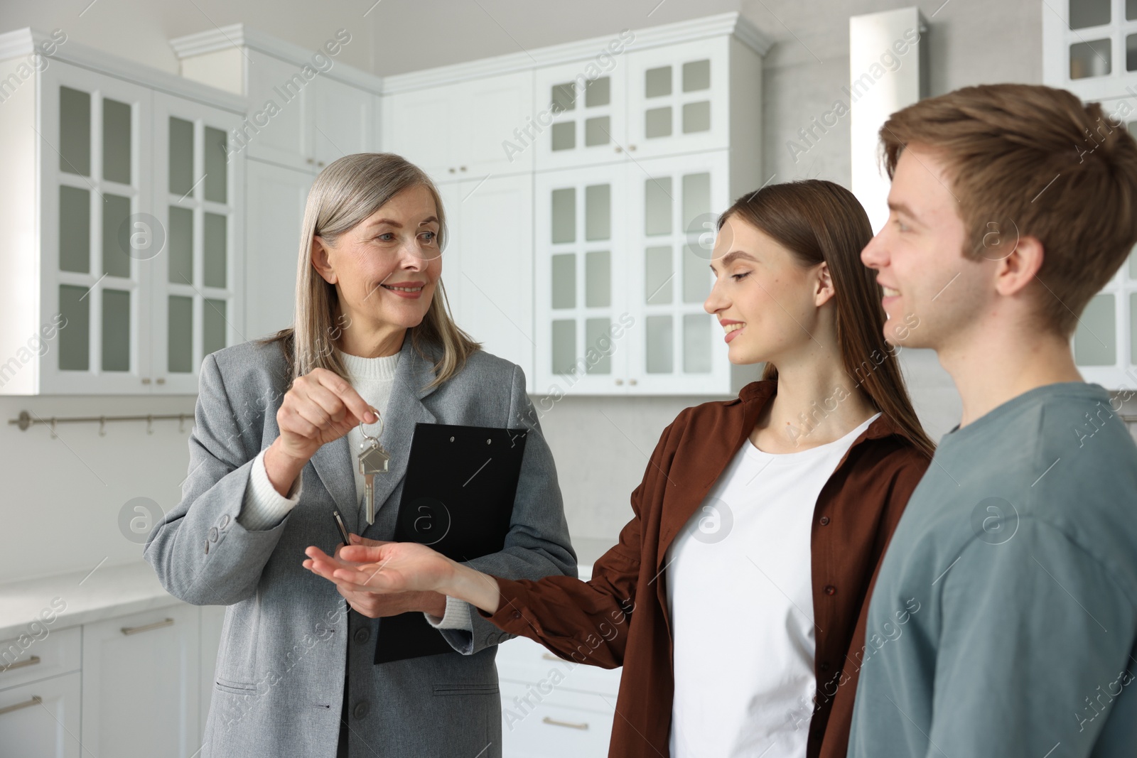 Smiling real estate agent giving house key to new owner in kitchen Photo of Smiling real estate agent giving house key to new owner in kitchen