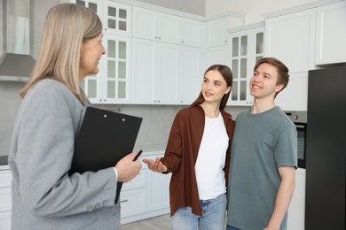 Photo of Real estate agent with clipboard working with couple in kitchen