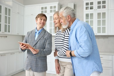 Photo of Smiling real estate agent with tablet working with couple in kitchen