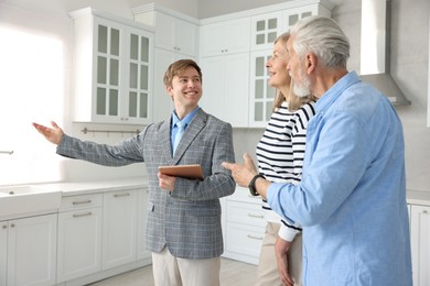 Photo of Smiling real estate agent with tablet working with couple in kitchen