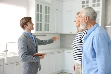 Photo of Smiling real estate agent with tablet working with couple in kitchen