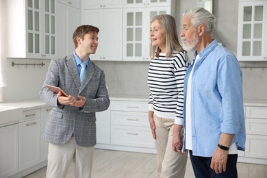 Photo of Smiling real estate agent with tablet working with couple in kitchen