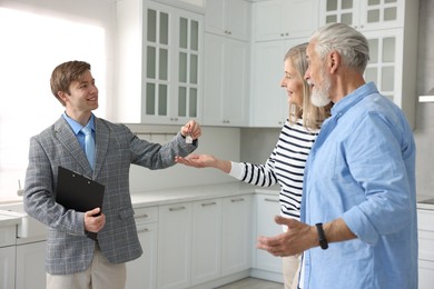 Photo of Smiling real estate agent giving house key to new owner in kitchen