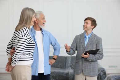Photo of Smiling real estate agent with clipboard working with couple at home