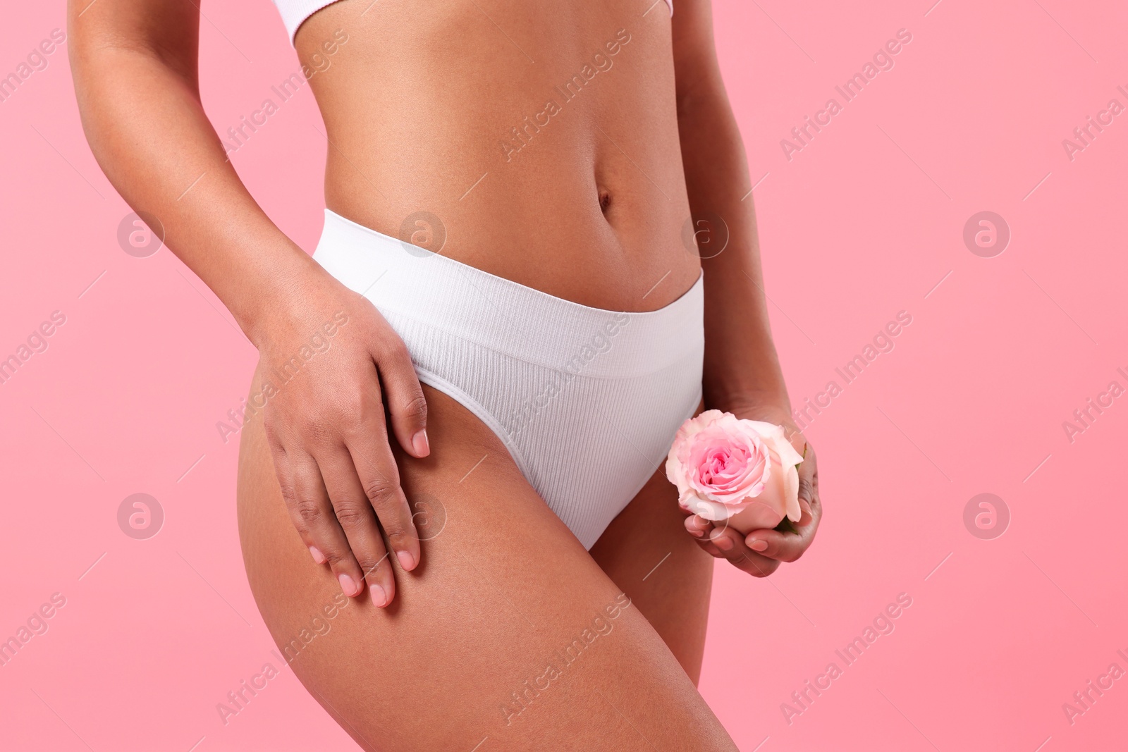 Woman in white underwear with flower showing smooth skin after epilation procedure on pink background, closeup Photo of Woman in white underwear with flower showing smooth skin after epilation procedure on pink background, closeup