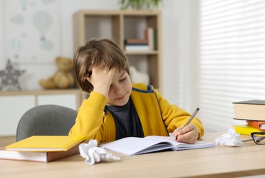 Photo of Tired little boy doing homework at table indoors